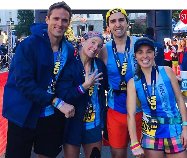 Four running athletes posing after a race with their medals around their necks.